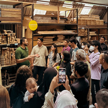 Group of people in a workshop or storage area with wooden shelves.